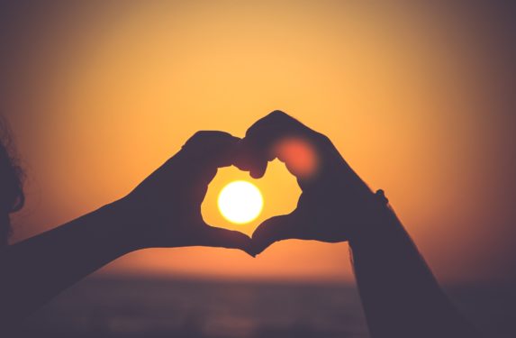 Image of hands in heart shape outlining sun in sunset